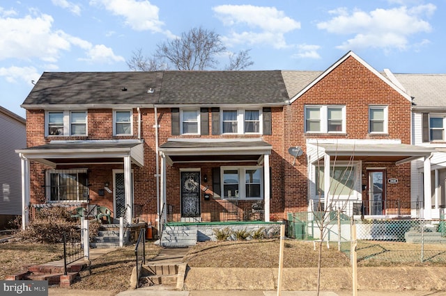 townhome / multi-family property with a porch, brick siding, and roof with shingles