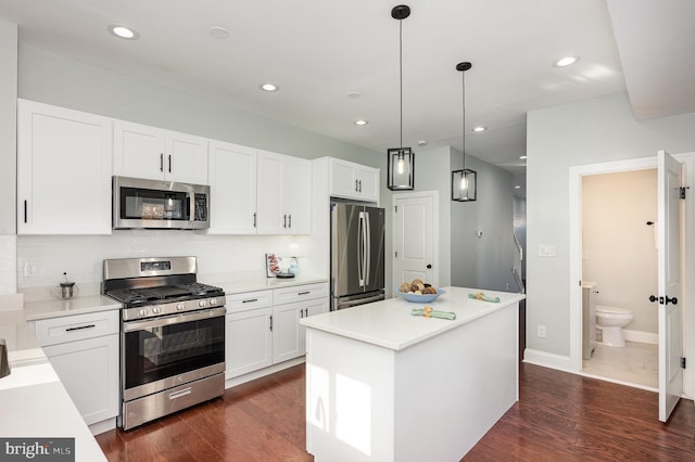 kitchen featuring appliances with stainless steel finishes, dark wood-type flooring, pendant lighting, white cabinets, and a center island