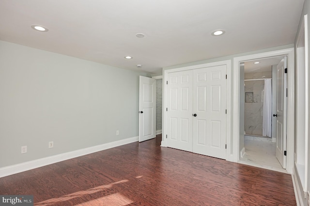 unfurnished bedroom with a closet, ensuite bathroom, and dark hardwood / wood-style flooring