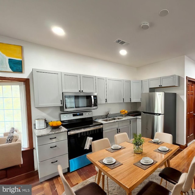 kitchen with gray cabinets, appliances with stainless steel finishes, light hardwood / wood-style floors, light stone countertops, and sink