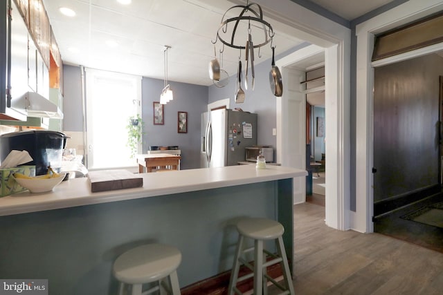 kitchen with pendant lighting, dark wood-type flooring, a kitchen breakfast bar, stainless steel fridge, and kitchen peninsula