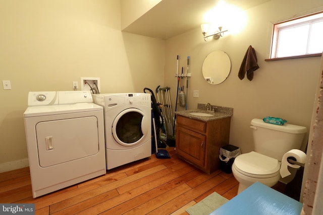 clothes washing area featuring washing machine and clothes dryer, sink, and light hardwood / wood-style floors