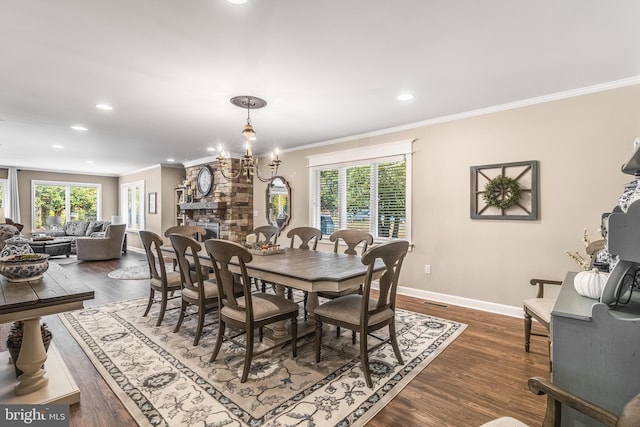 dining area featuring a chandelier, dark hardwood / wood-style floors, a stone fireplace, and ornamental molding