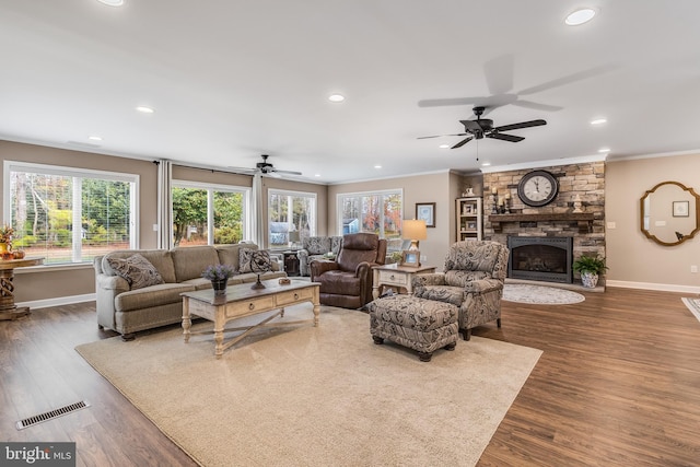 living room featuring a stone fireplace, crown molding, plenty of natural light, and dark wood-type flooring