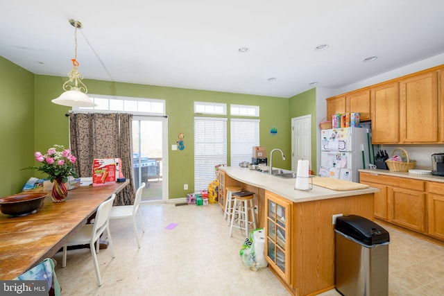 kitchen featuring sink, white fridge, pendant lighting, a breakfast bar area, and a kitchen island with sink