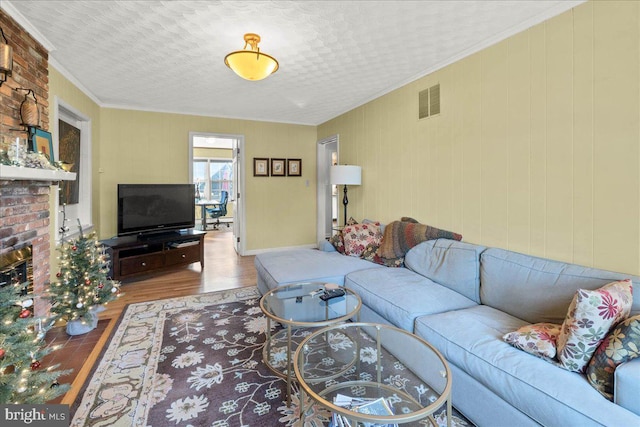 living room featuring crown molding, wood-type flooring, a textured ceiling, and a brick fireplace