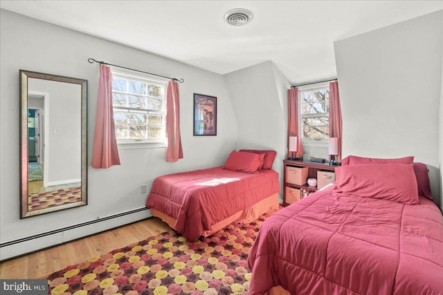 bedroom featuring hardwood / wood-style flooring, baseboard heating, and multiple windows