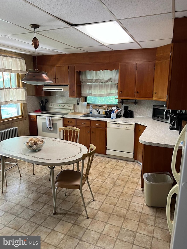 kitchen with radiator heating unit, sink, hanging light fixtures, ventilation hood, and white appliances