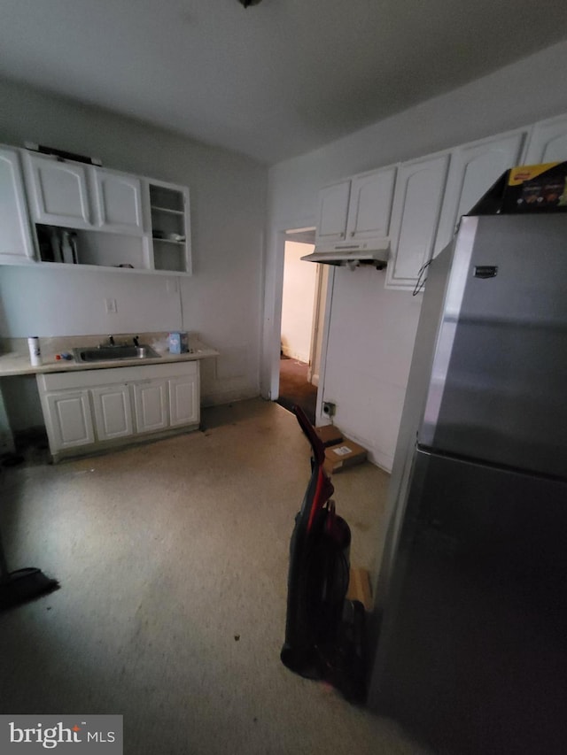 kitchen with stainless steel fridge, light colored carpet, white cabinetry, and sink