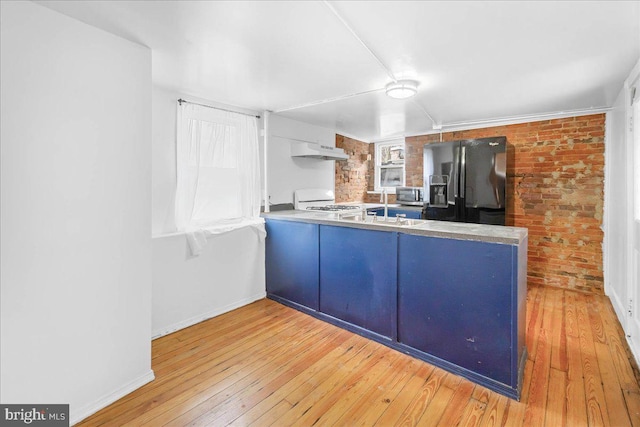 kitchen with black fridge, white range, light wood-type flooring, kitchen peninsula, and brick wall