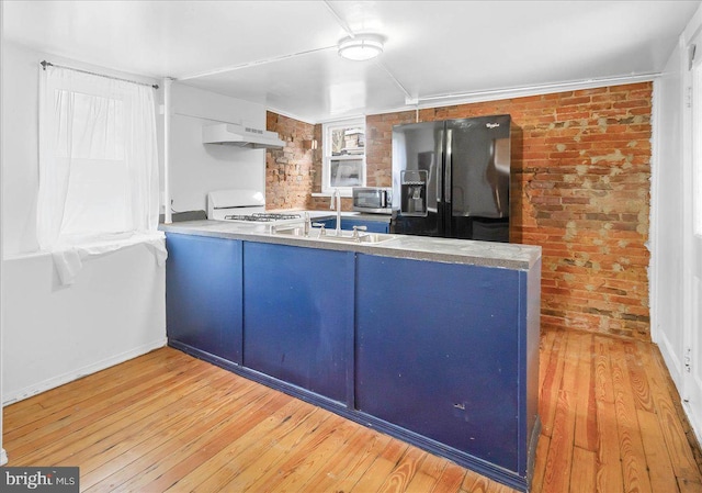 kitchen with black fridge, light hardwood / wood-style flooring, brick wall, kitchen peninsula, and white stove