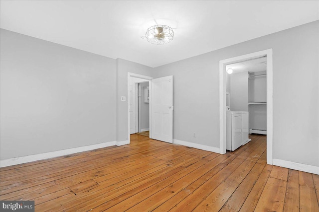 unfurnished bedroom with a baseboard radiator, separate washer and dryer, light hardwood / wood-style flooring, a walk in closet, and a closet