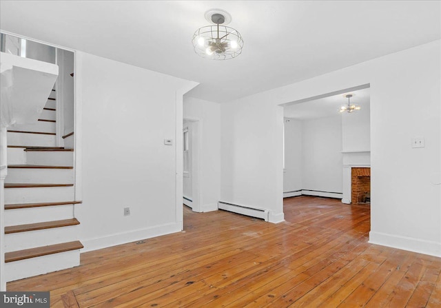 unfurnished living room featuring a brick fireplace, a notable chandelier, baseboard heating, and light hardwood / wood-style flooring