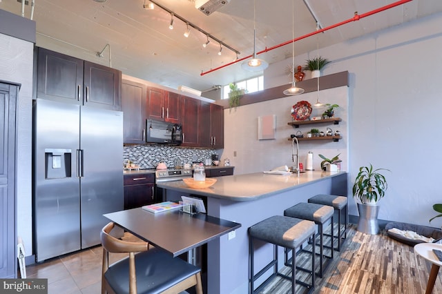 kitchen with stainless steel refrigerator with ice dispenser, decorative backsplash, decorative light fixtures, a kitchen bar, and kitchen peninsula