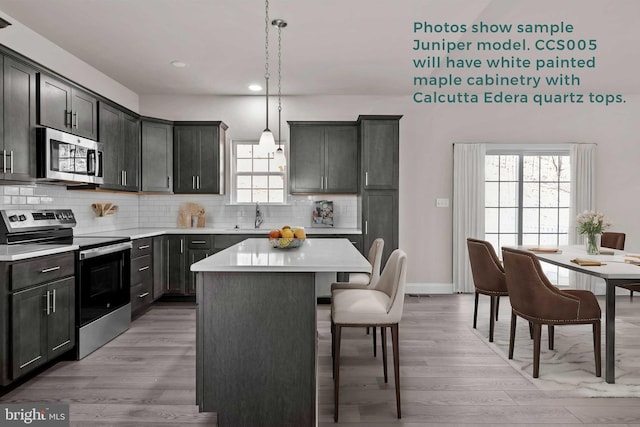 kitchen with a breakfast bar area, stainless steel appliances, light countertops, decorative backsplash, and light wood finished floors