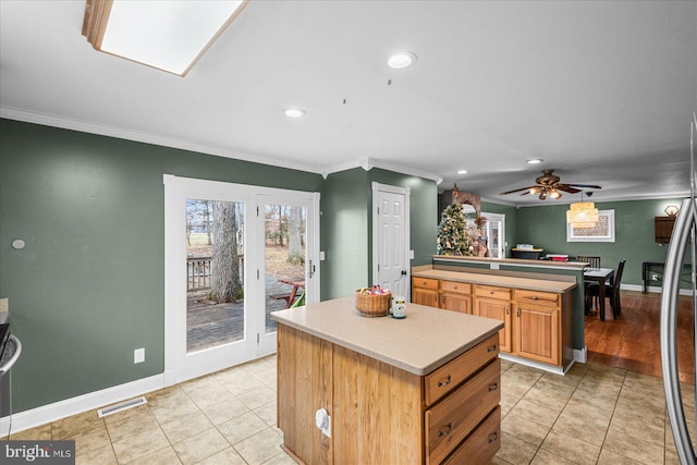 kitchen with light tile patterned floors, a kitchen island, ceiling fan, and crown molding