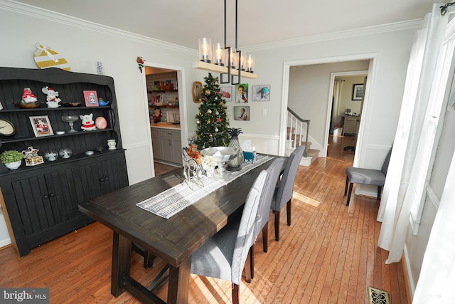 dining area with ornamental molding, a notable chandelier, and hardwood / wood-style flooring