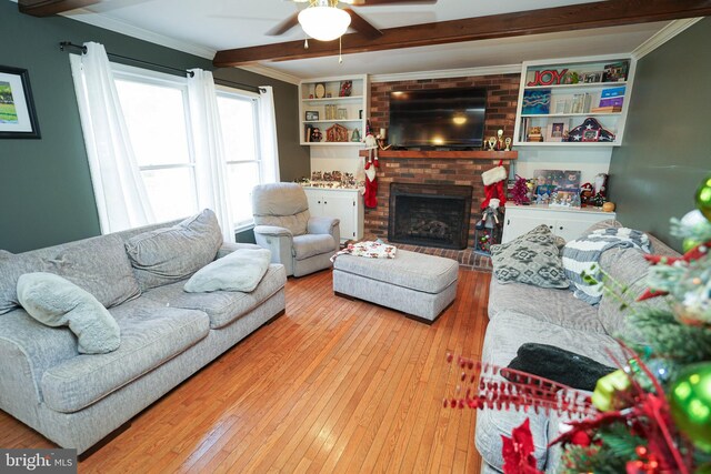 living room featuring a brick fireplace, ceiling fan, crown molding, beam ceiling, and hardwood / wood-style floors