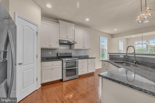 kitchen with appliances with stainless steel finishes, white cabinets, sink, a chandelier, and range hood