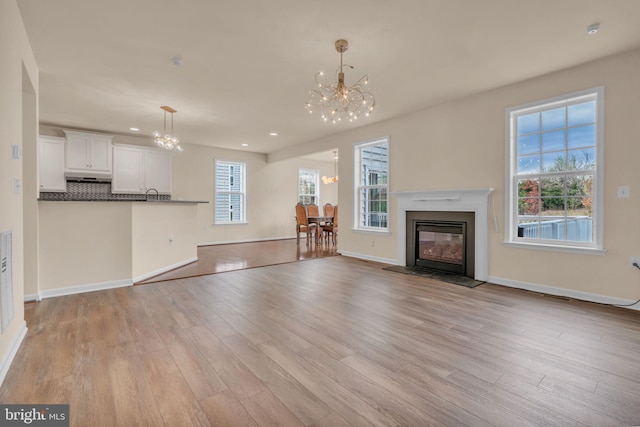 unfurnished living room featuring plenty of natural light, a notable chandelier, and light hardwood / wood-style flooring