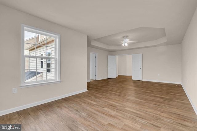 unfurnished room with a raised ceiling, ceiling fan, and light hardwood / wood-style floors