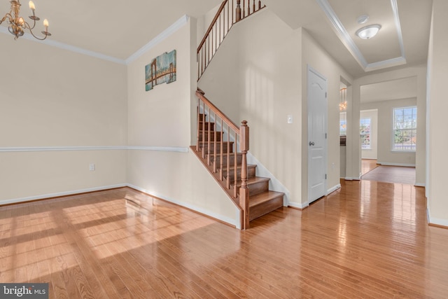 entryway with wood-type flooring, crown molding, and a notable chandelier