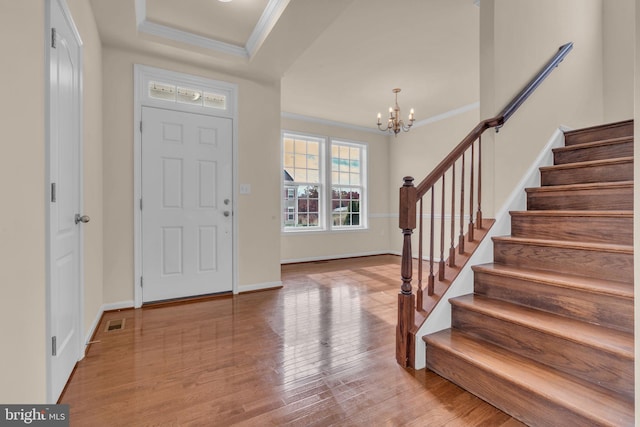 foyer with a raised ceiling, a chandelier, light hardwood / wood-style floors, and ornamental molding