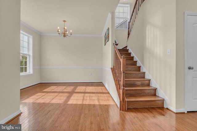 staircase featuring wood-type flooring, crown molding, and a chandelier