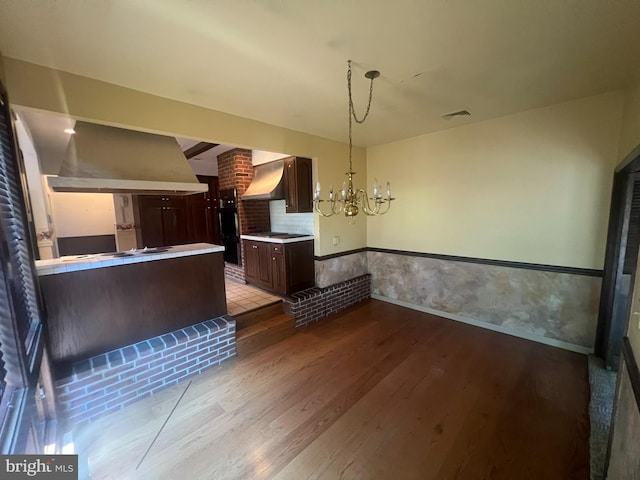 kitchen with dark brown cabinetry, hanging light fixtures, premium range hood, hardwood / wood-style floors, and a chandelier