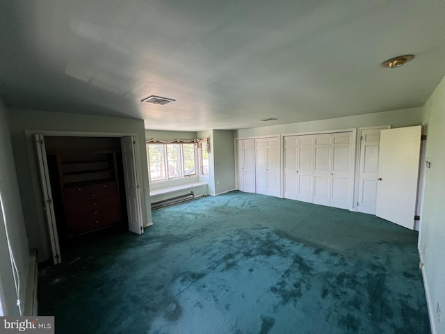 unfurnished bedroom featuring dark colored carpet, baseboard heating, and two closets