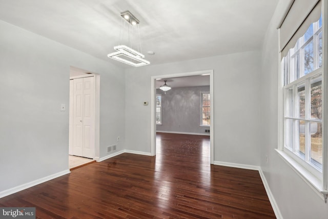 empty room featuring a notable chandelier and dark wood-type flooring