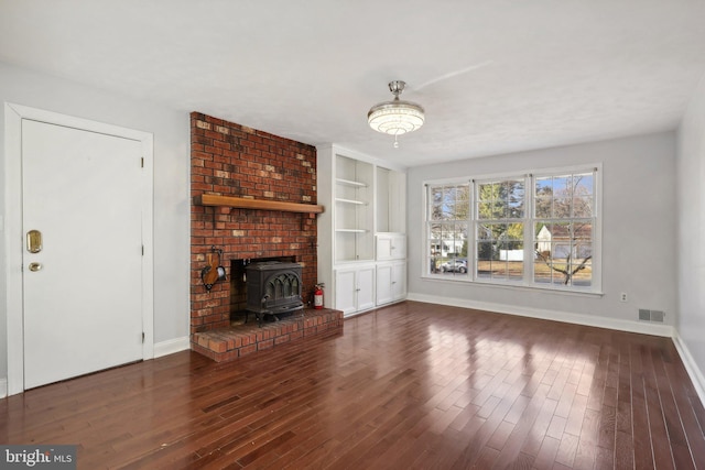 unfurnished living room with a wood stove, built in shelves, and dark hardwood / wood-style floors