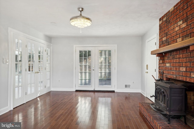 unfurnished living room featuring plenty of natural light, dark hardwood / wood-style flooring, a wood stove, and french doors