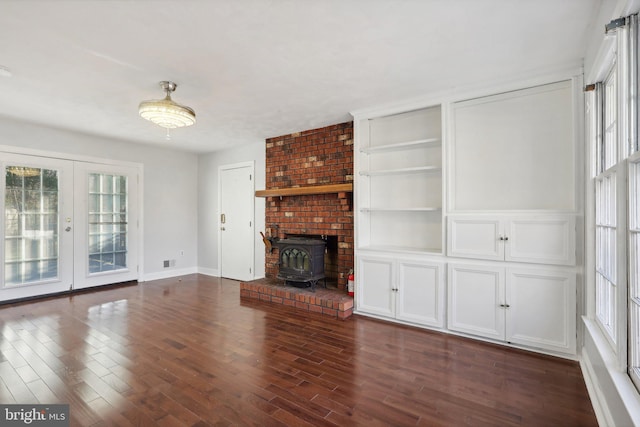 unfurnished living room with built in shelves, a wood stove, dark hardwood / wood-style flooring, and french doors