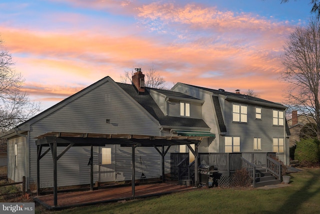 back house at dusk featuring a deck and a lawn