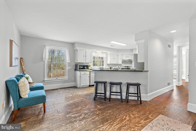 kitchen featuring a kitchen bar, kitchen peninsula, stainless steel dishwasher, dark wood-type flooring, and white cabinets