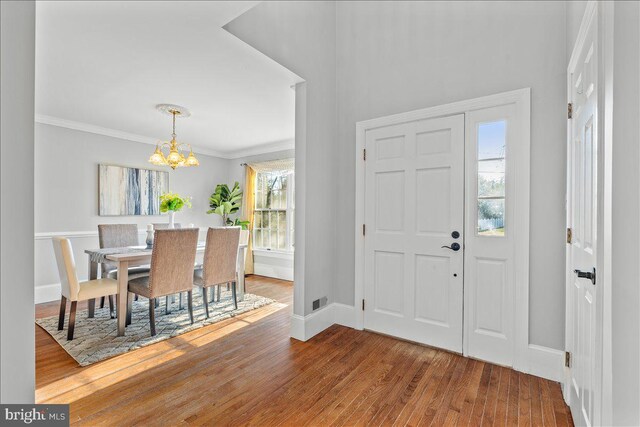 foyer entrance with a chandelier, ornamental molding, a healthy amount of sunlight, and wood-type flooring