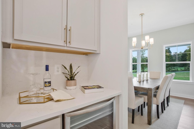 kitchen with white cabinetry, an inviting chandelier, wine cooler, light hardwood / wood-style flooring, and pendant lighting