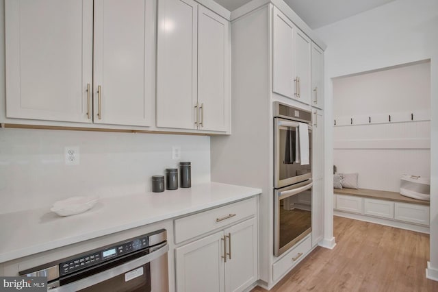 kitchen with white cabinets, double oven, and light hardwood / wood-style flooring