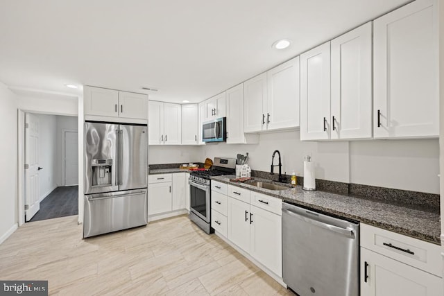 kitchen featuring appliances with stainless steel finishes, white cabinetry, dark stone countertops, and sink