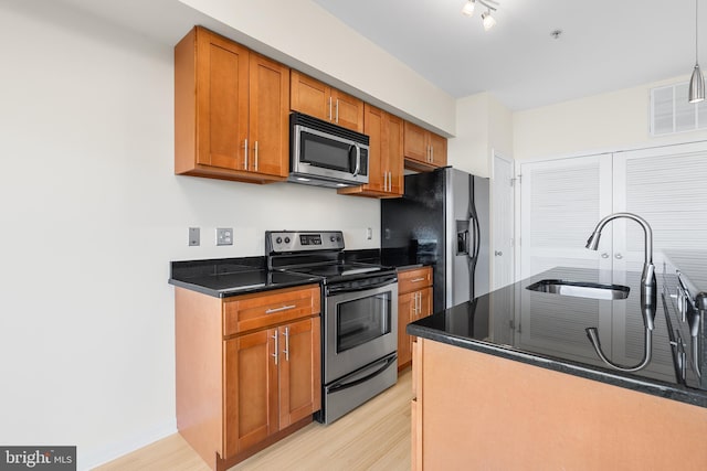 kitchen with decorative light fixtures, stainless steel appliances, light hardwood / wood-style floors, and sink