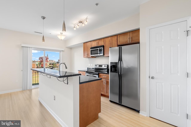 kitchen with a center island with sink, hanging light fixtures, appliances with stainless steel finishes, light hardwood / wood-style floors, and a breakfast bar area