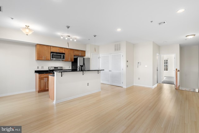 kitchen with a kitchen breakfast bar, stainless steel appliances, light hardwood / wood-style floors, hanging light fixtures, and an island with sink