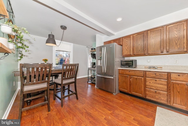 kitchen featuring beam ceiling, stainless steel fridge with ice dispenser, hardwood / wood-style floors, pendant lighting, and decorative backsplash