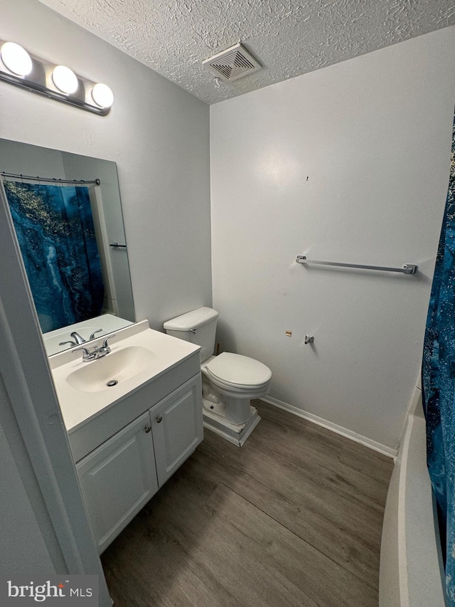 bathroom with hardwood / wood-style floors, vanity, toilet, and a textured ceiling