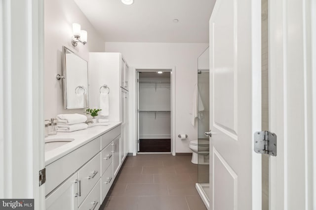 bathroom featuring tile patterned flooring, a walk in closet, toilet, double vanity, and a sink