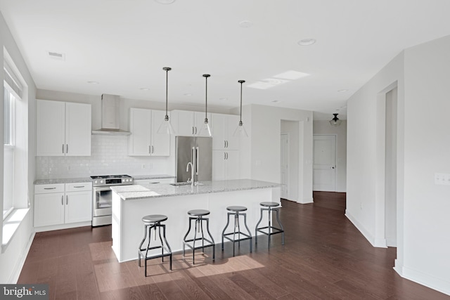 kitchen featuring dark wood-type flooring, a breakfast bar, a kitchen island with sink, appliances with stainless steel finishes, and wall chimney exhaust hood