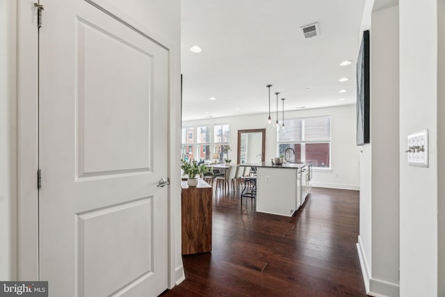 hallway featuring visible vents, baseboards, dark wood-style flooring, recessed lighting, and a sink