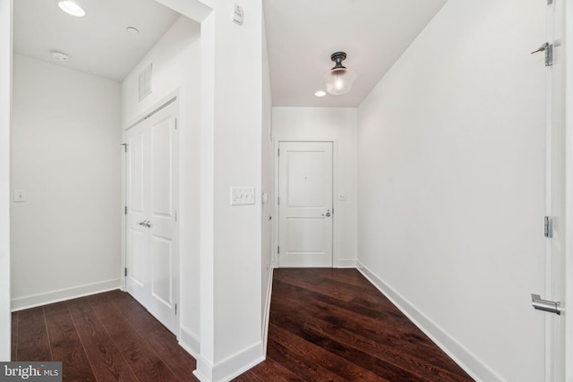 hall featuring visible vents, baseboards, and dark wood-style flooring