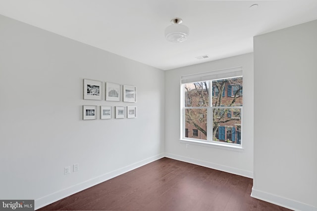 spare room featuring baseboards, visible vents, and dark wood-style flooring